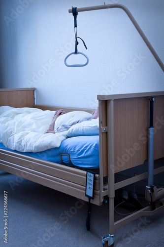 Dead person with extremly thin arms and joined hands in a nursing bed at home or in a hospice room, conept of death, blue filter effect photo