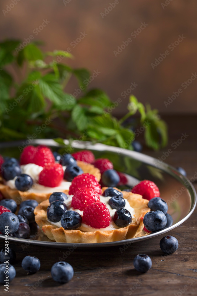 Dessert tarts with raspberries and blueberries on a wooden table. Dessert tarts with raspberries and blueberries on a wooden table.