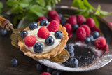  Dessert tarts with raspberries and blueberries on a wooden table.