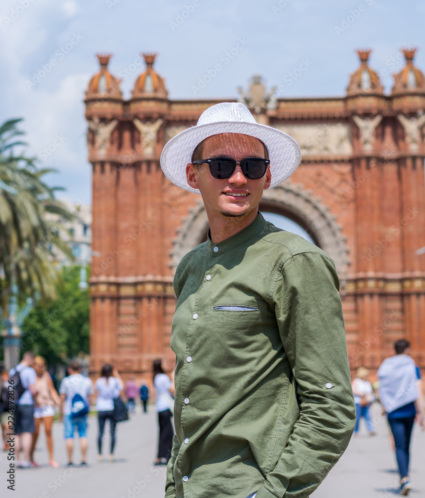 A young guy, a tourist in glasses stands and smiles near the Arc de Triomf in the city of Barcelona, Spain