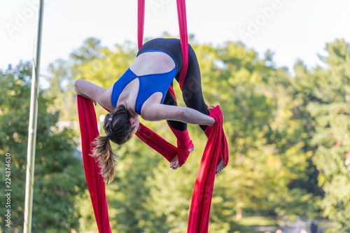 A lady in blue and black fitness outfit is hanging on a red ribbon is attempting to tied red ribbon on her legs.