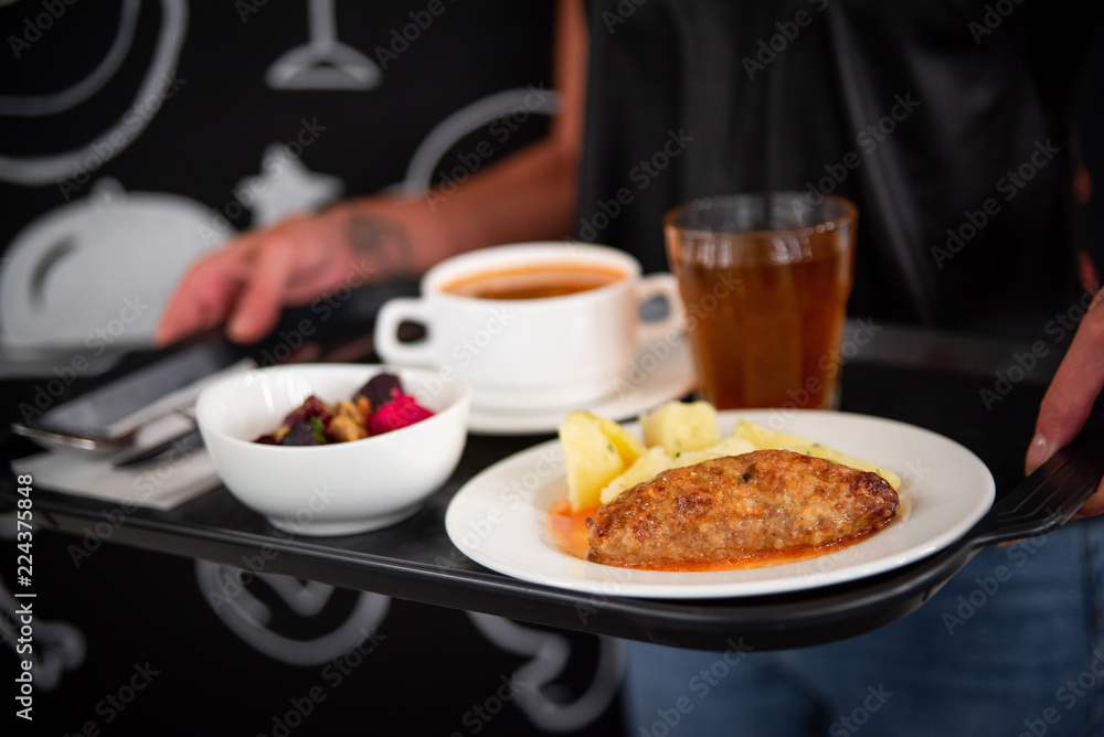 The girl holds a tray in the dining room, on a salad tray, a hot dish, compote, soup. Девушка держит поднос в столовой, на подносе салат, горячее блюдо, компот, суп.
