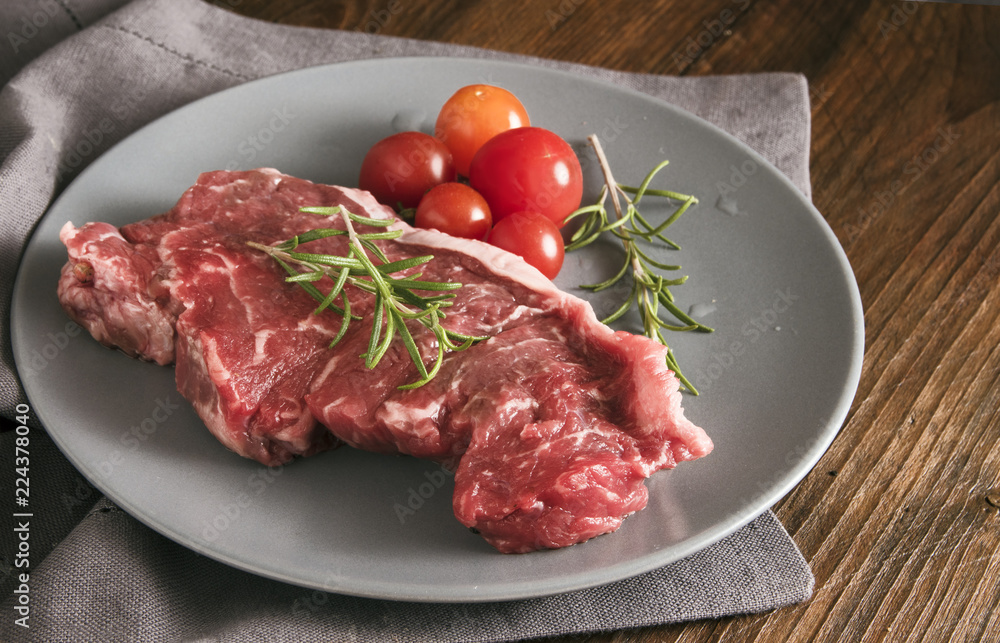 raw steak with rosemary and tomatoes on a gray plate on rustic wood raw steak with rosemary and tomatoes on a gray plate on rustic wood