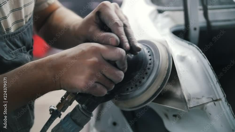 The mechanic's hands grind the car body with a grinder The mechanic's hands grind the car body with a grinder