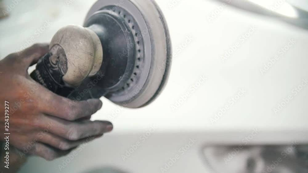 The mechanic's hand holds the grinder and turns it off The mechanic's hand holds the grinder and turns it off