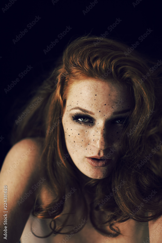 Beautiful young woman with red hair and freckles portrait, beauty shoot on dark background, mysterious dark mood Beautiful young woman with red hair and freckles portrait, beauty shoot on dark background, mysterious dark mood