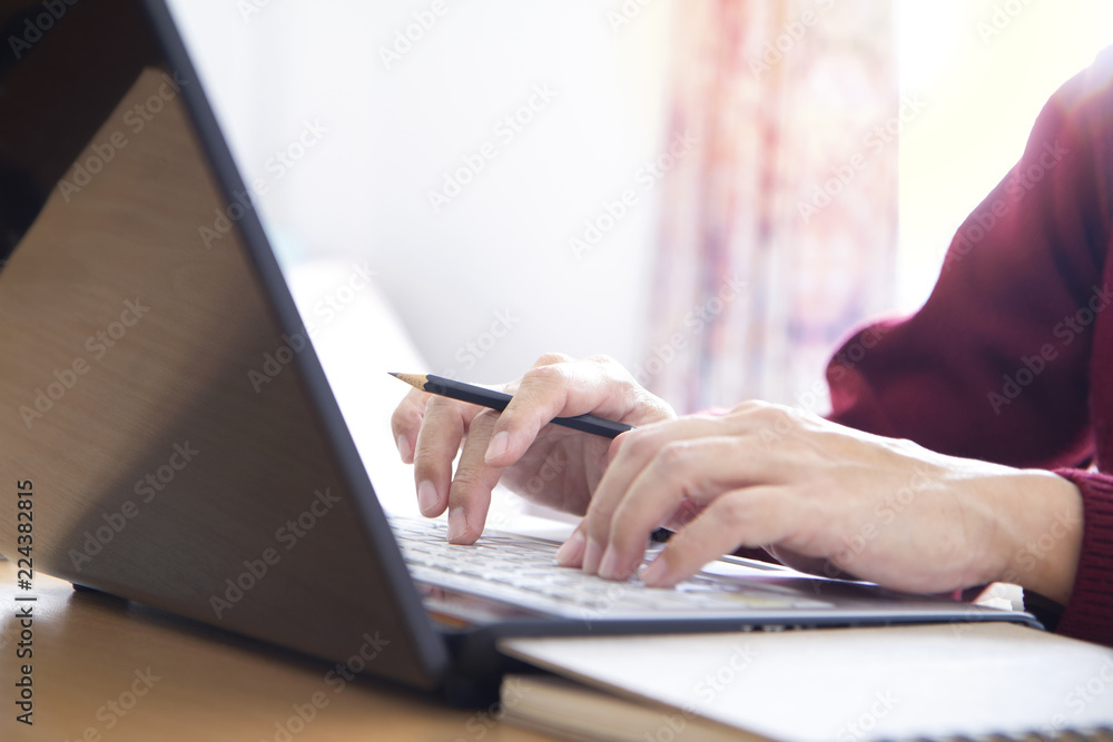 Hands of a man in red sweater holding a pencil while typing on laptop computer notebook keyboard in the office. Closeup with left and top copy space and easy to be cropped as a banner or strip. Hands of a man in red sweater holding a pencil while typing on laptop computer notebook keyboard in the office. Closeup with left and top copy space and easy to be cropped as a banner or strip.