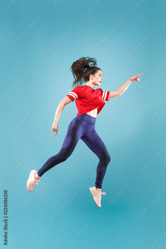 Obraz premium I am happy. Mid-air shot of pretty smiling young woman jumping and gesturing against pink studio background. Runnin girl in motion or movement. Human emotions and facial expressions concept
