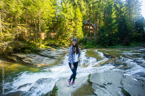 Young woman on edge of rock near fast river in middle of forest