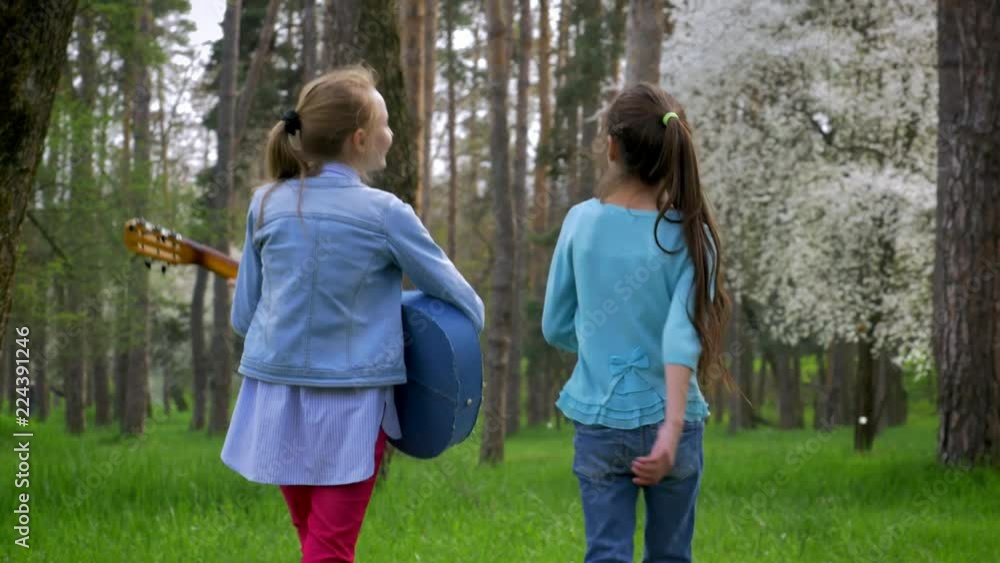 pure nature Park in springtime. Two little Caucasian girl go on foot with guitar in hand on the forest path. concept of environment pure nature Park in springtime. Two little Caucasian girl go on foot with guitar in hand on the forest path. concept of environment