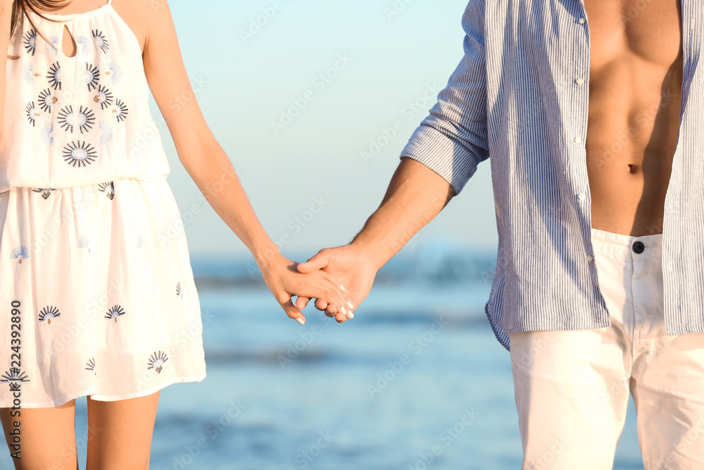 Happy young couple holding hands at beach on sunny day, closeup Happy young couple holding hands at beach on sunny day, closeup