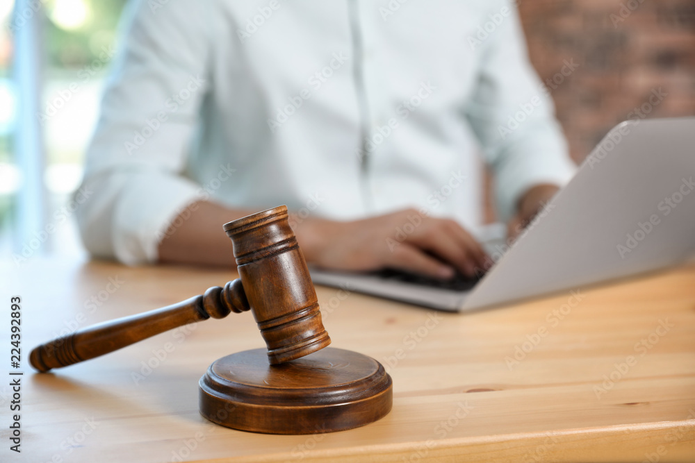Wooden gavel and blurred notary with laptop on background Wooden gavel and blurred notary with laptop on background