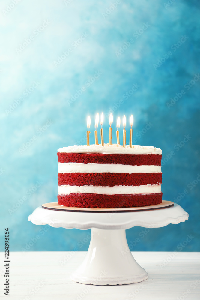 Delicious homemade red velvet cake with candles on table against color  background Stock Photo | Adobe Stock