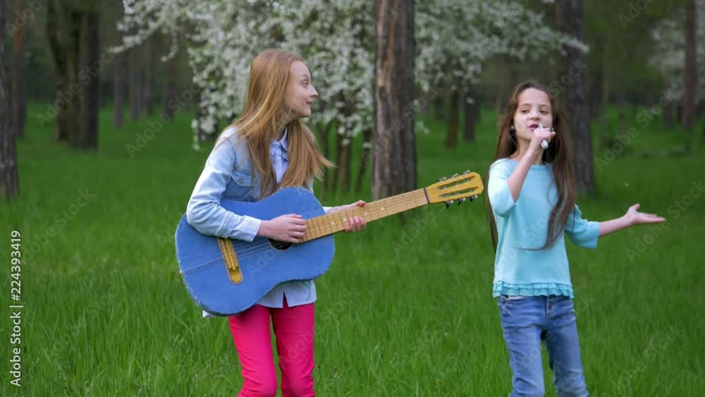 imitation pop musician performance in the forest Park Happy little girlfriends fool around dancing and sing songs playing guitar.shaking long her hair head. springtime imitation pop musician performance in the forest Park Happy little girlfriends fool around dancing and sing songs playing guitar.shaking long her hair head. springtime