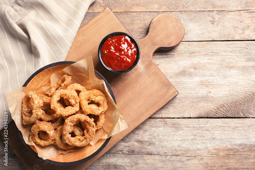 Homemade crunchy fried onion rings in plate and sauce on wooden background, top view. Space for text