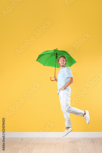 Man with green umbrella near color wall