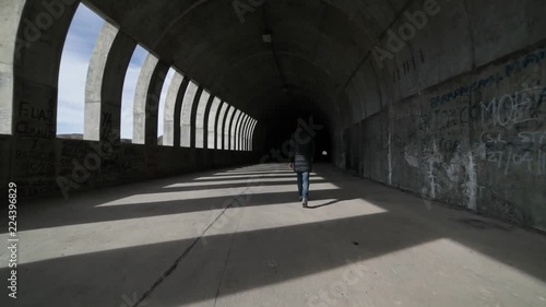 Hand held camera woman walking towards and getting in a brutalist concrete tunnel. Lights and shadows rithms made by windows, openings, within the tunnel. Street infraestructure. Argentina, Mendoza photo