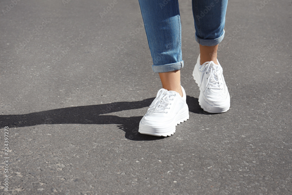 Woman in stylish sneakers walking outdoors, focus on legs