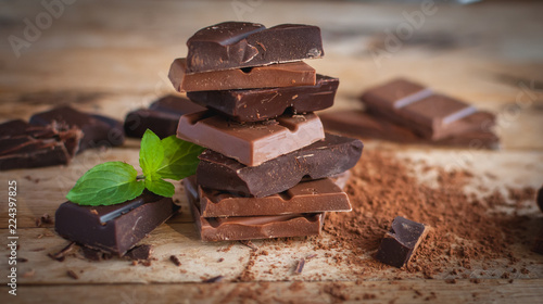 Close-up of stacked dark and milk chocolate with fresh mint on wooden background 