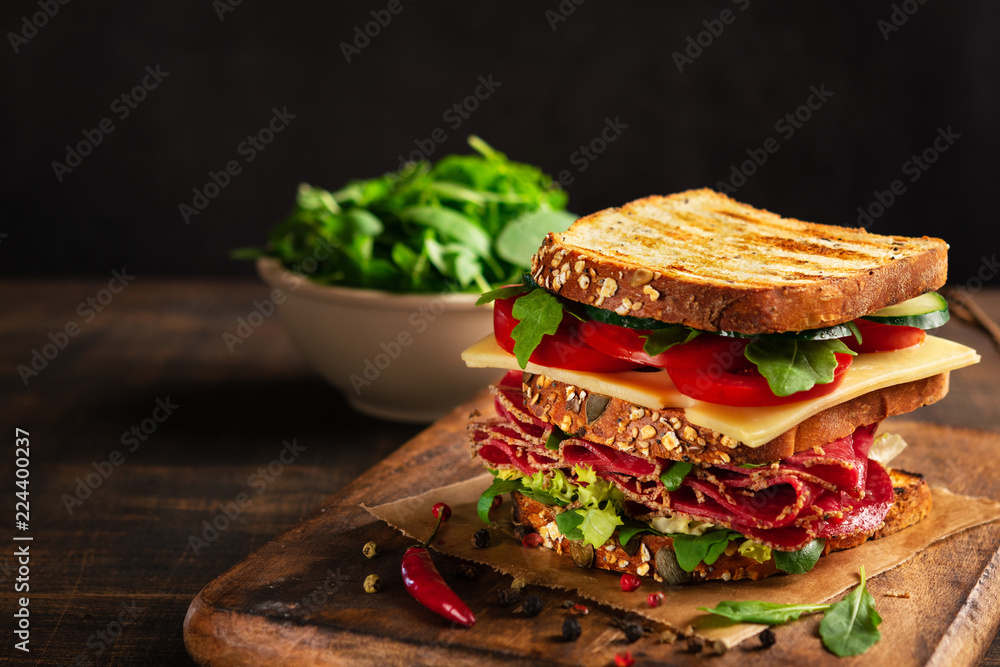 Φωτογραφία Close-up of delicious Sandwich with salami, cheese and fresh vegetables on rustic wooden cutting board on wooden table, selective focus