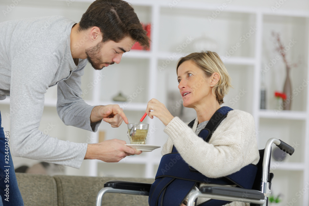 caregiver giving cup of tea to disabled woman in wheelchair caregiver giving cup of tea to disabled woman in wheelchair