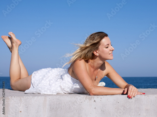 Foto Barefoot young woman in short white sleeveless dress sunbathes with eyes closed