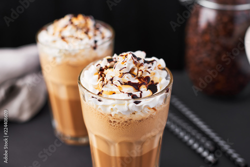Iced latte coffee in a tall glass with caramel and chocolate syrup and whipped cream.