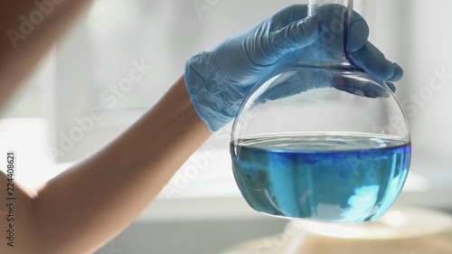 Close-up of a flask in a laboratory experiment, with blue liquid swirling into the flask. HD