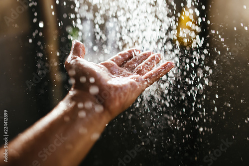 A man's hand in a spray of water in the sunlight against a dark background. Water as a symbol of purity and life photo