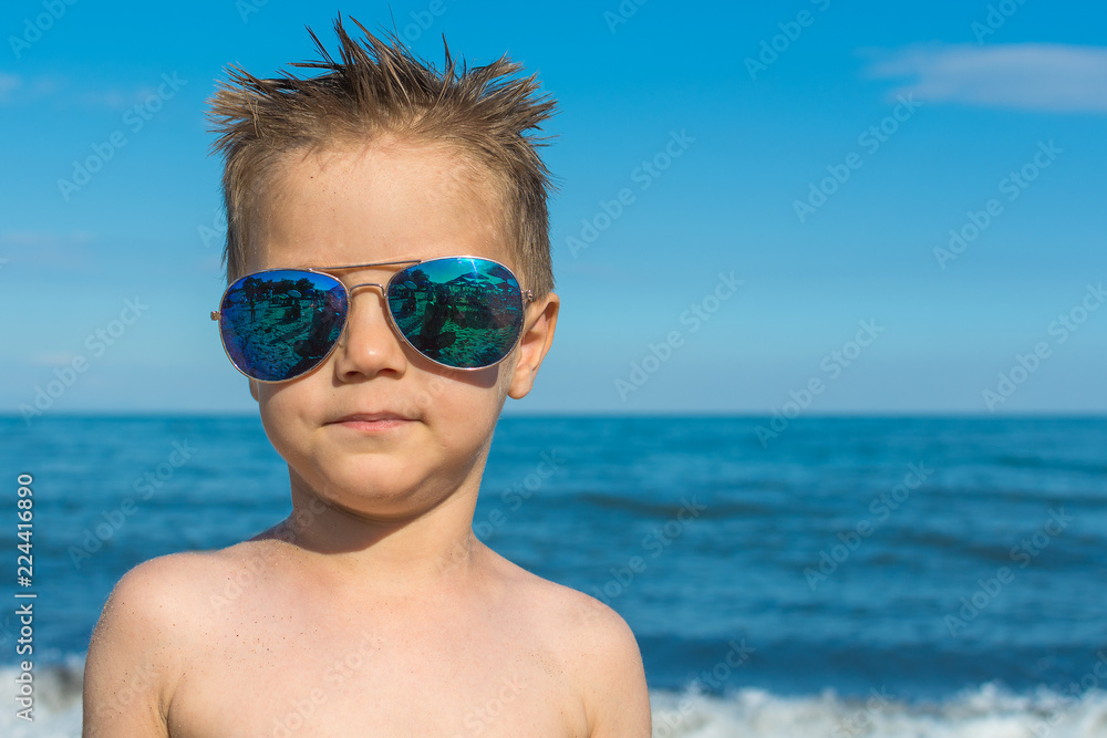 a beautiful little boy posing on a beach by the sea with sunglasses a beautiful little boy posing on a beach by the sea with sunglasses