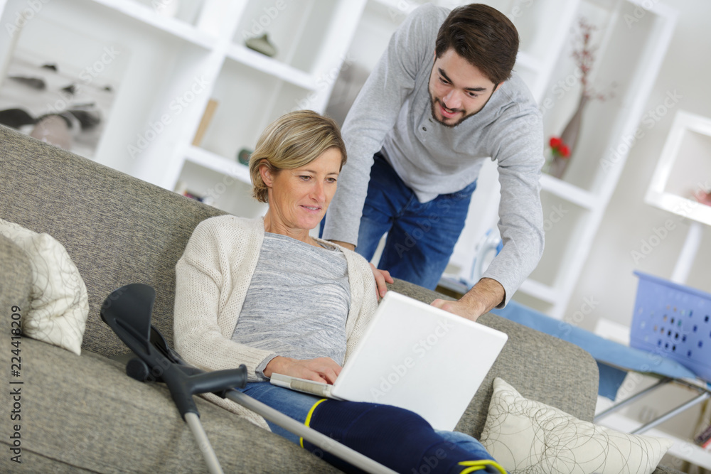 Obraz premium middle-age woman injured sitting on the sofa and using laptop