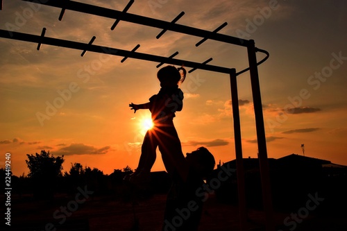 father raises high his little daughter in the hands of the children's playground is the bright evening sun