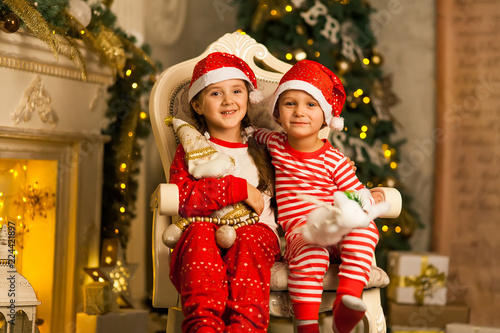 Happy children sit together on a chair near the Christmas tree