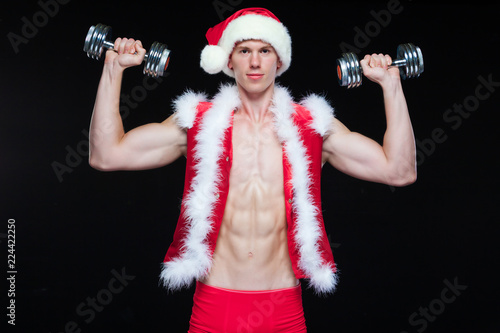 Holidays and celebrations, New year, Christmas, sports, bodybuilding, healthy lifestyle - Muscular handsome Santa Claus. on a black background with dumbbells. Isolated on white background.