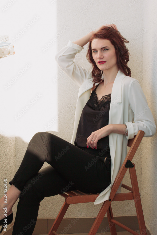 Beautiful redhear woman white jacket, high heels, and black shirt sitting the balcone Beautiful redhear woman white jacket, high heels, and black shirt sitting the balcone