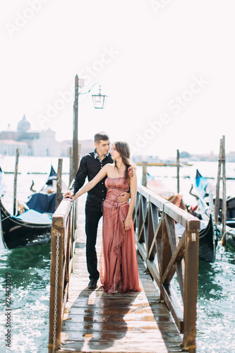 couple of pretty young woman and handsome man are standing by the canal with gondolas in Venice, Italy. © sofiko14