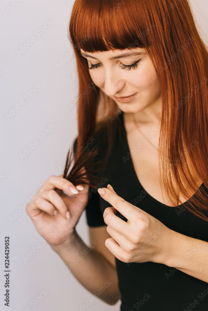 Obraz premium red-haired woman looks at the tips of the hair in her hand in the studio. Close-up