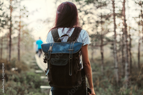 Back view of a tourist girl with backpack walk on a wooden footpath in beautiful forest.