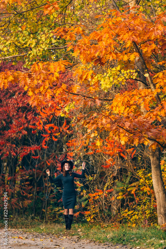 dark-haired girl in a hat smiles and holds branches of trees by her hands in the park in the autumn