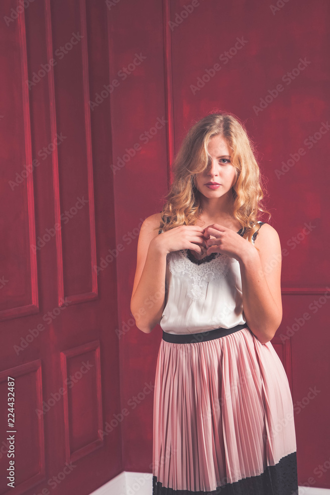 Fashion young woman in silk dress on red studio background. A beautiful, sexy girl with blonde hair and cute face in the studio on a red background. Beautiful girl with long wavy hair.