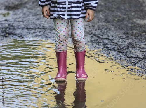 Playful child outdoor jump into puddle in boot after rain 