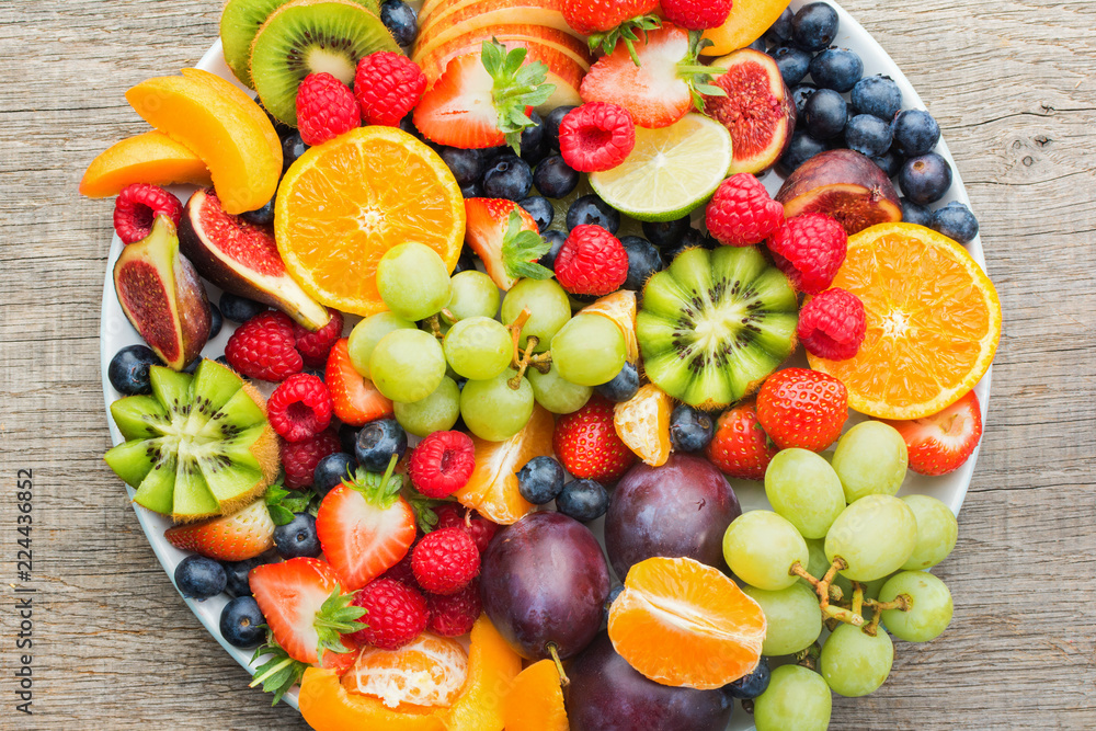 Healthy fruit platter, strawberries raspberries oranges plums apples kiwis grapes blueberries on the dark grey wooden table, top view, close up, selective focus