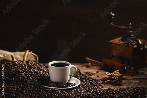 Coffee beans white cup of fragrant coffee and coffee grinder on wooden table on black background