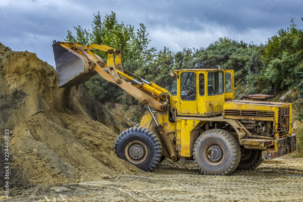 Wheel loader Excavator with backhoe unloading sand at eathmoving works in construction site quarry Wheel loader Excavator with backhoe unloading sand at eathmoving works in construction site quarry