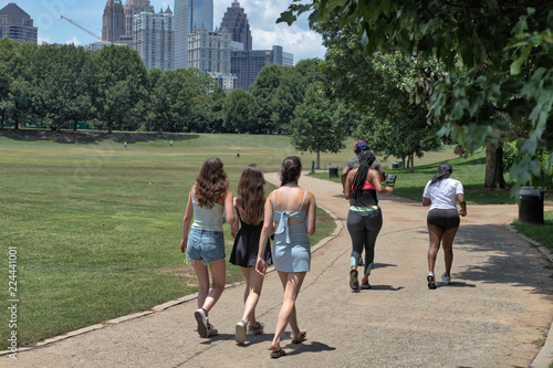 Fototapeta Naklejka Na Ścianę i Meble -  Unidentifiable walkers and runners on a path at Piedmont Park in Atlanta, GA on a hot summer day with buildings in the distance