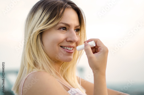 Closeup of beautiful natural young adult woman applying lip balm