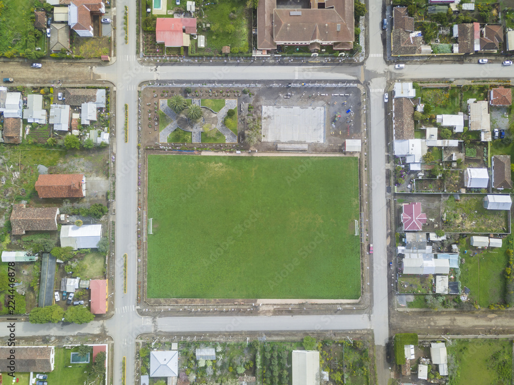 An aerial view of Chile countryside from the drone, a small grass football field as the Main Square inside a new and symmetrical urban planning of the streets in the town of Buchupureo, Chile