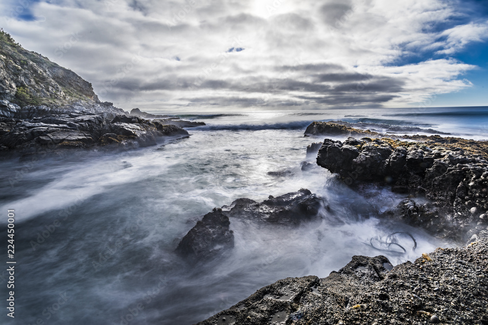 A long exposure shot of the sea at Puertecillo Beach with a dramatic sky full of clouds and the motion movement of the waves inside the water below the rocks. An amazing sky reflected on water. Chile