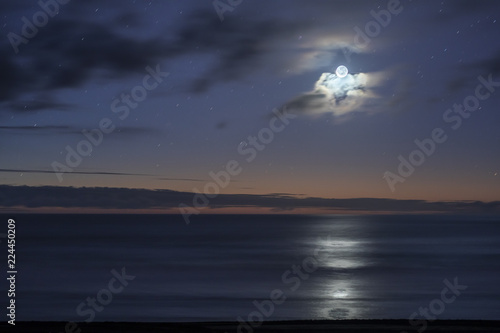 A crescent moon iluminates the coastline and sea landscape during twilight hour at 