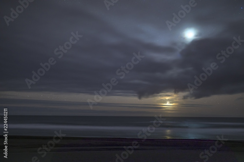 A crescent moon iluminates the coastline and sea landscape during twilight hour at 